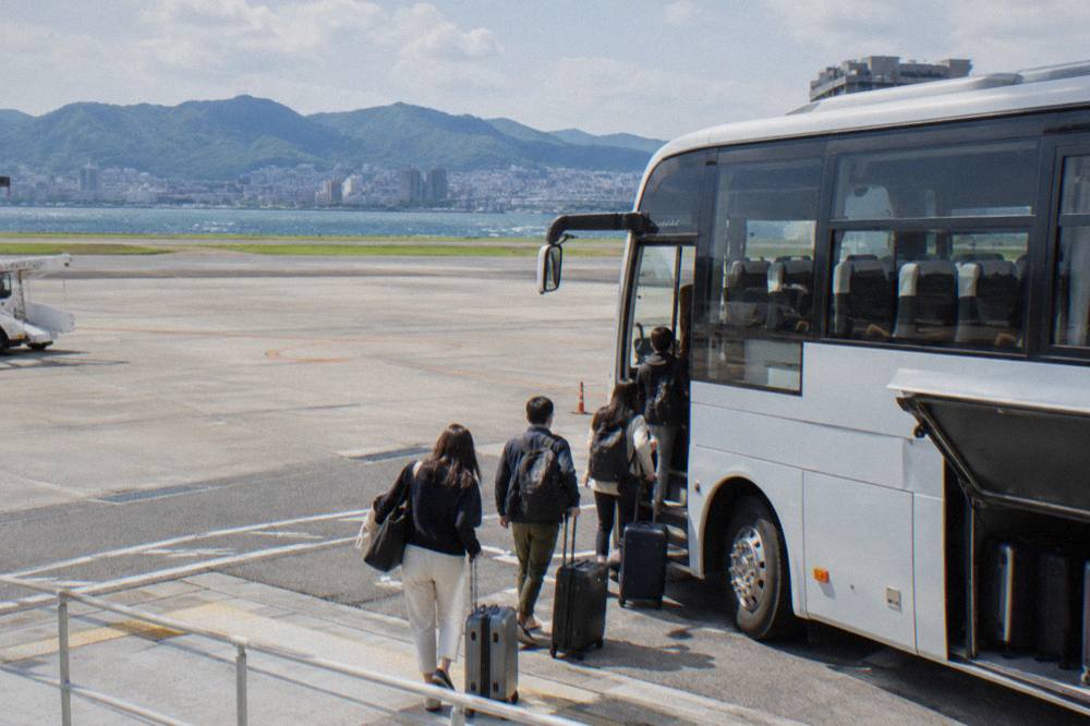 Passengers with suitcases boarding a long-distance coach at an airport platform