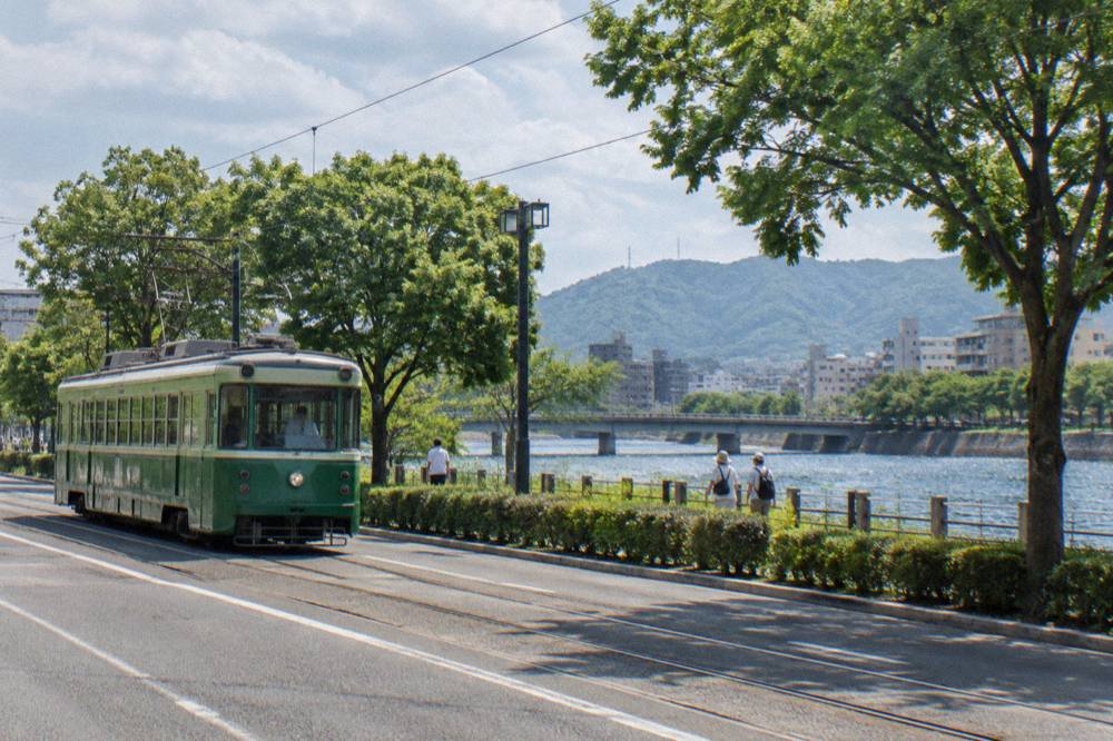A Hiroden streetcar in green livery passing through a Hiroshima street in the early morning