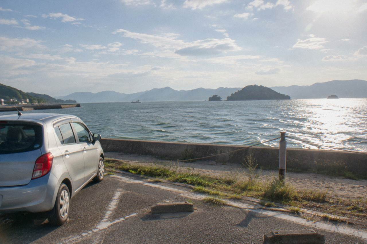 A rental car parked at a seaside lot with islands of the Seto Inland Sea in the background