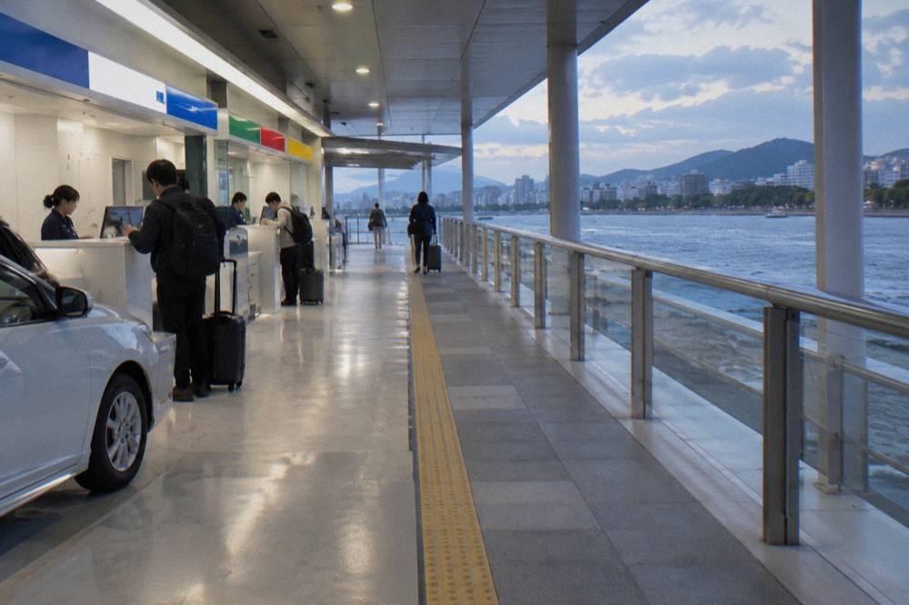 A bright rental car counter hall with staffed desks and a walkway leading toward an airport terminal