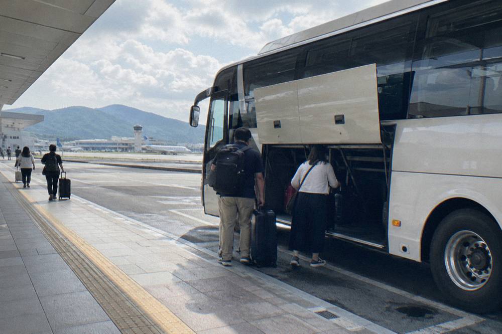 A limousine bus pulled up at an airport curb with passengers loading luggage aboard