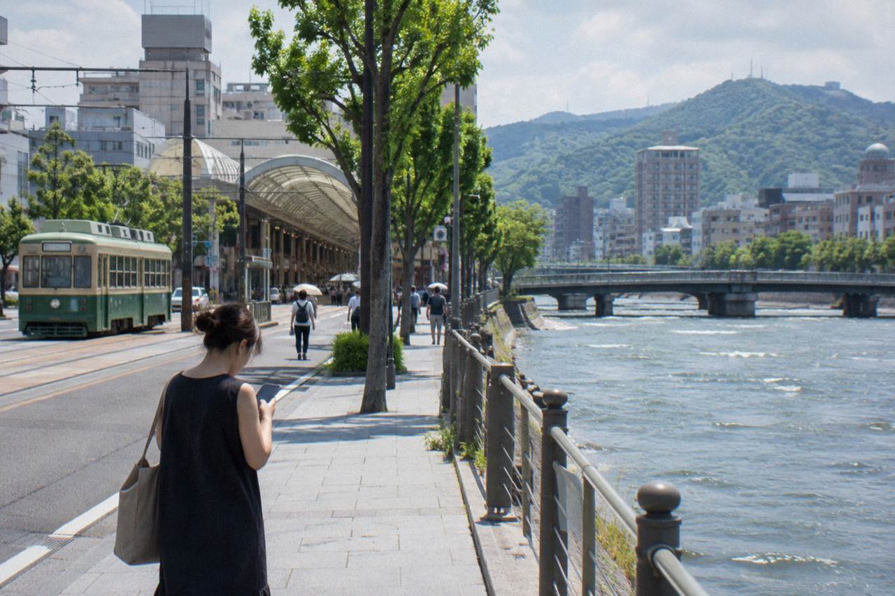 A traveller checking a smartphone on a Hiroshima street with trams and covered shopping arcade in the background