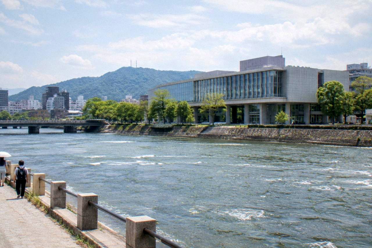 The modern concrete facade of a history museum beside a river in Hiroshima
