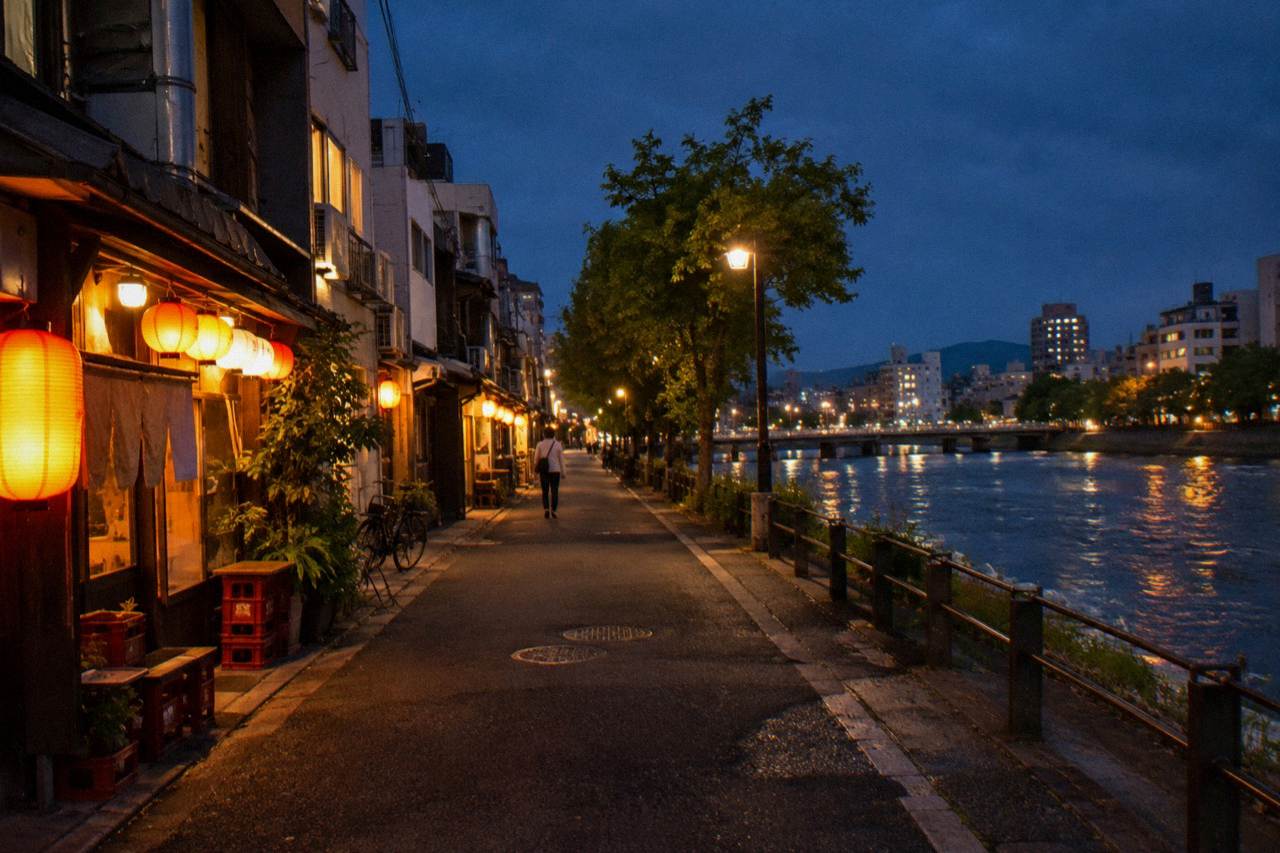 Glowing paper lanterns and warm window light brighten a narrow lane of small izakaya bars at night