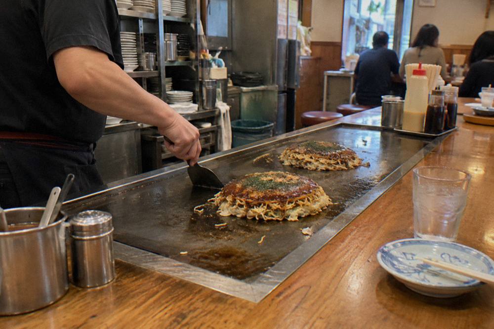Okonomiyaki cooking on a teppan at a small Hiroshima restaurant counter