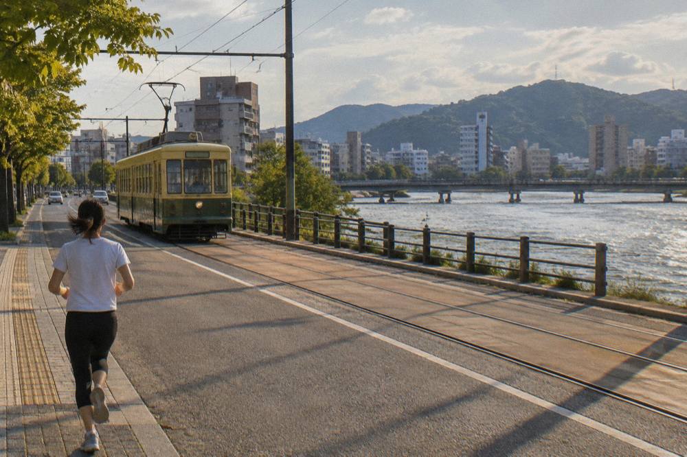 A green Hiroden streetcar travelling along a street in Hiroshima with passengers waiting to board