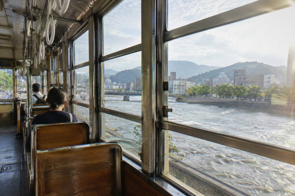 Interior of a Hiroden streetcar with wooden benches and hanging straps