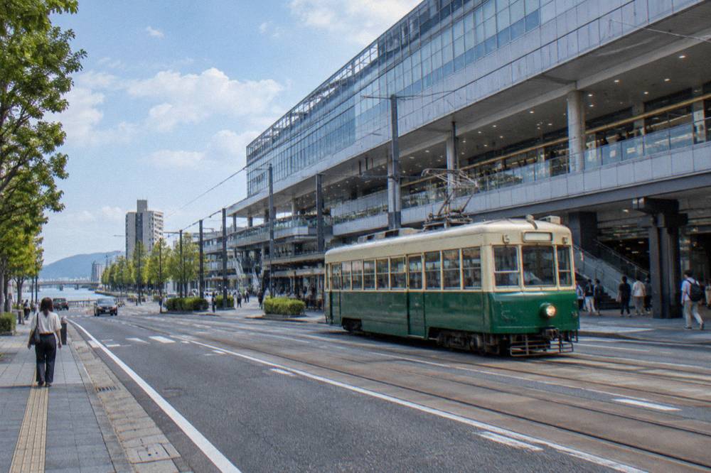 A green streetcar travelling along a city street past shopfronts