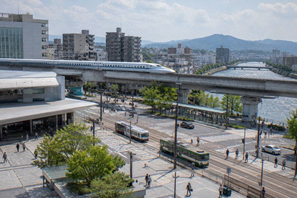 A long white bullet train speeding along an elevated track past city apartment blocks
