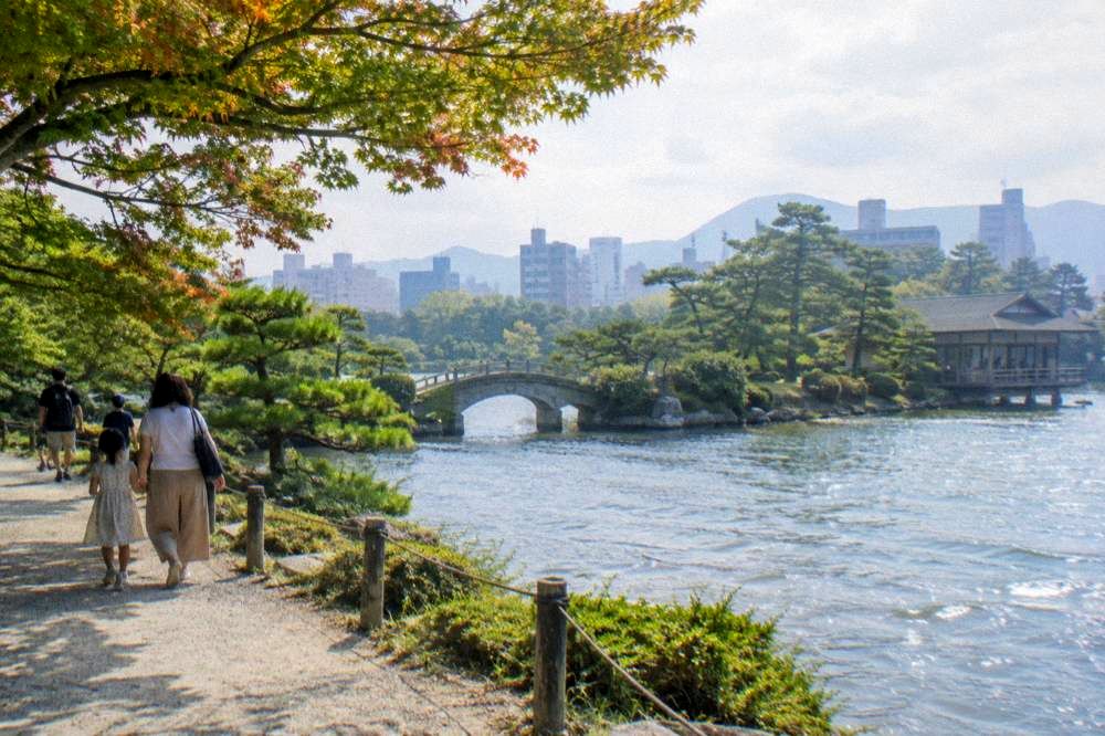 Families walking a pond path under maples inside Shukkeien garden in Hiroshima