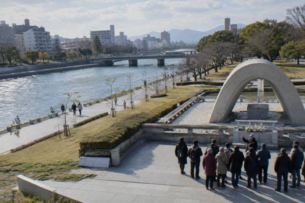 A tour group listening to a guide beside the cenotaph in Hiroshima Peace Memorial Park