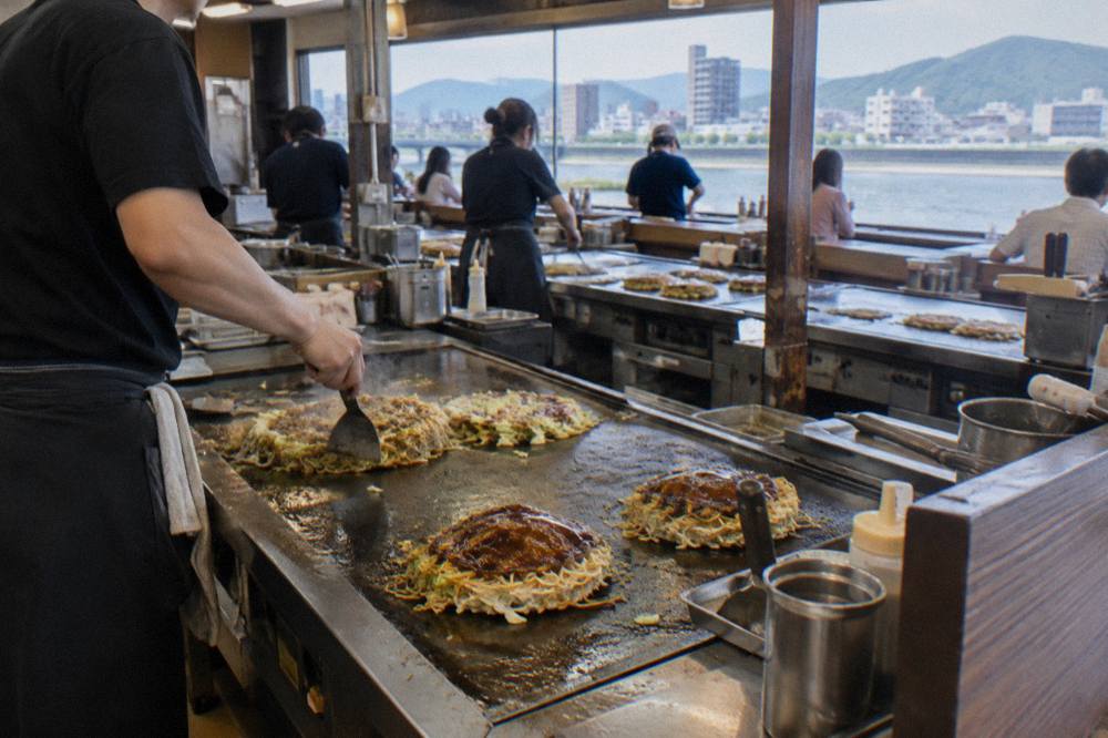 Rows of small okonomiyaki griddle counters inside a busy food building in Hiroshima