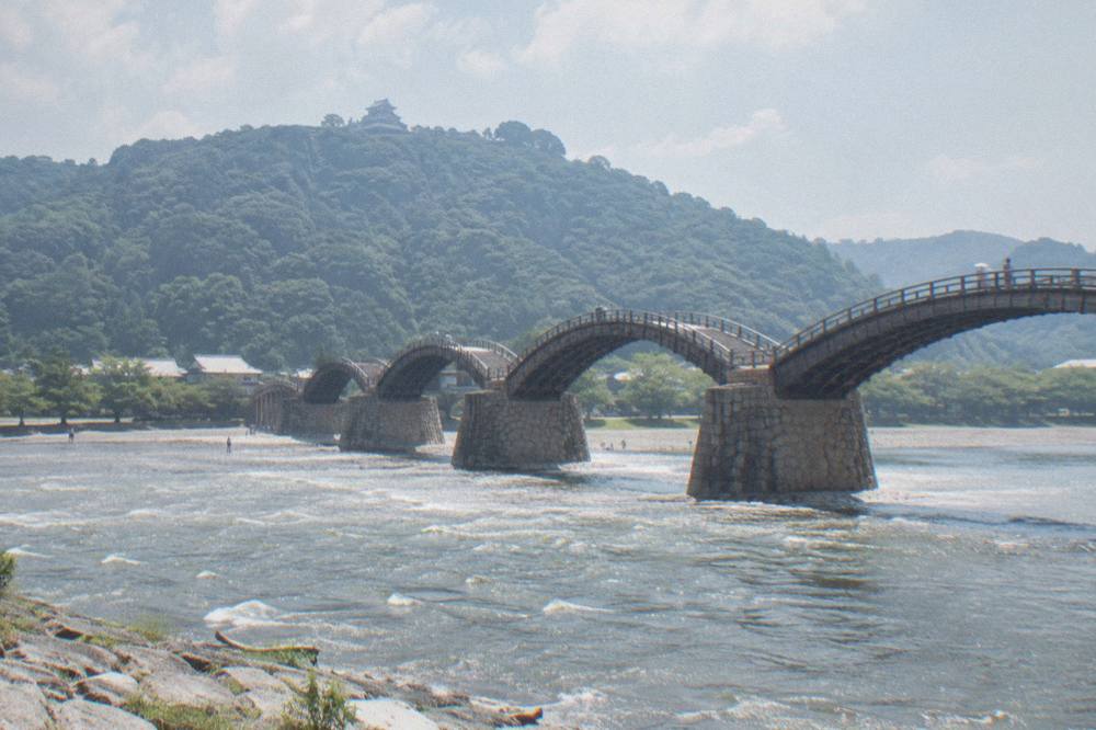 The wooden arches of Kintaikyo Bridge span a wide river with green hills rising behind.