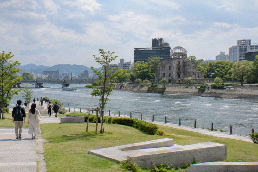 Visitors walk quiet paths through Peace Memorial Park toward the A-Bomb Dome across the river.