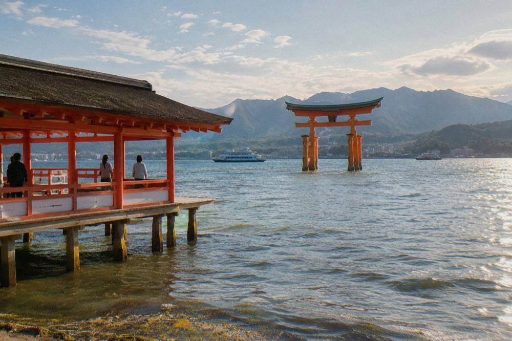 The great vermilion torii of Itsukushima Shrine rises from the shallows as ferries cross the water.