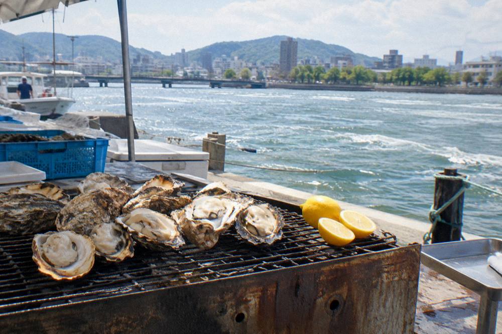 Plump grilled oysters rest on a hot grill beside lemon halves at a market stall.