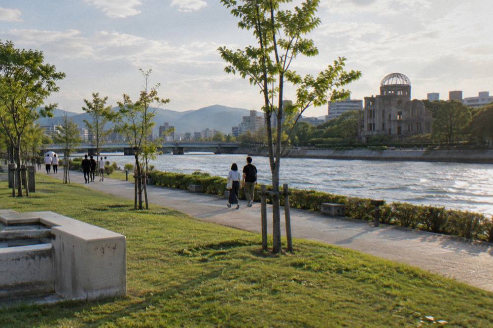 Visitors walk quietly along the tree lined paths of Hiroshima Peace Memorial Park on a clear morning.