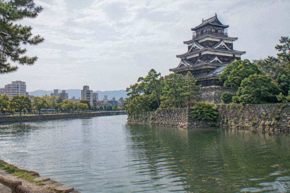 Hiroshima Castle keep rising above its stone walls and moat, viewed from the outer grounds.