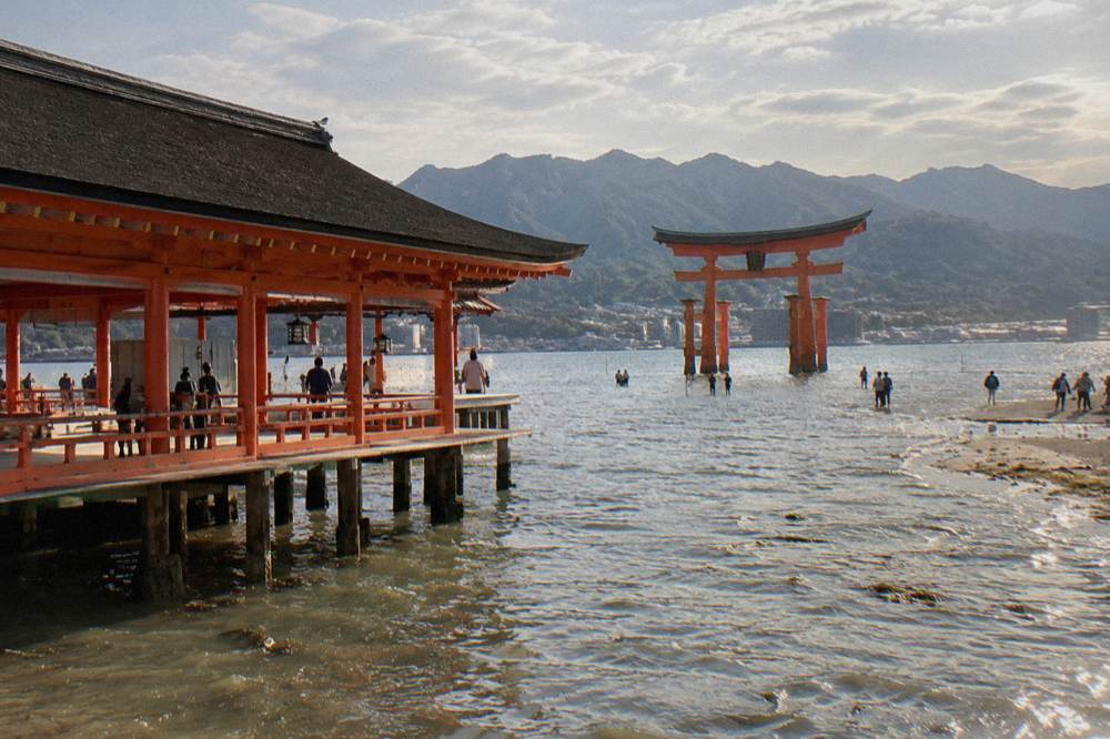 The great red torii of Itsukushima Shrine standing in the shallows at Miyajima with visitors on the shore.