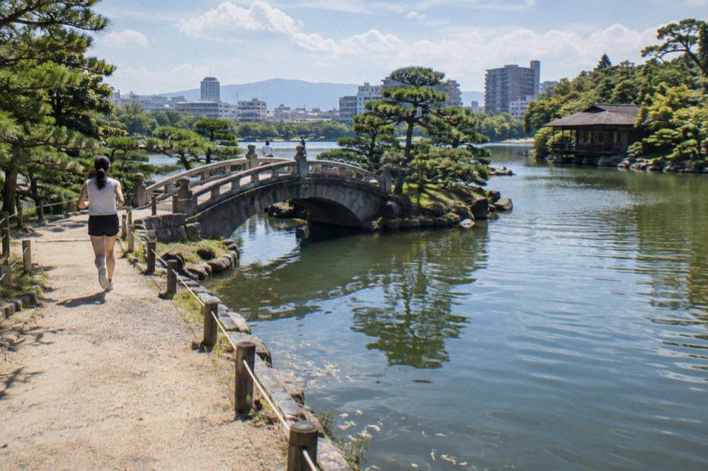 Stone bridge and pine trees reflected in a pond at Shukkeien Garden on a clear afternoon.