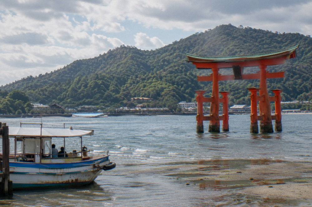 The red Great Torii rising from the water at low tide with forested Mount Misen behind it.