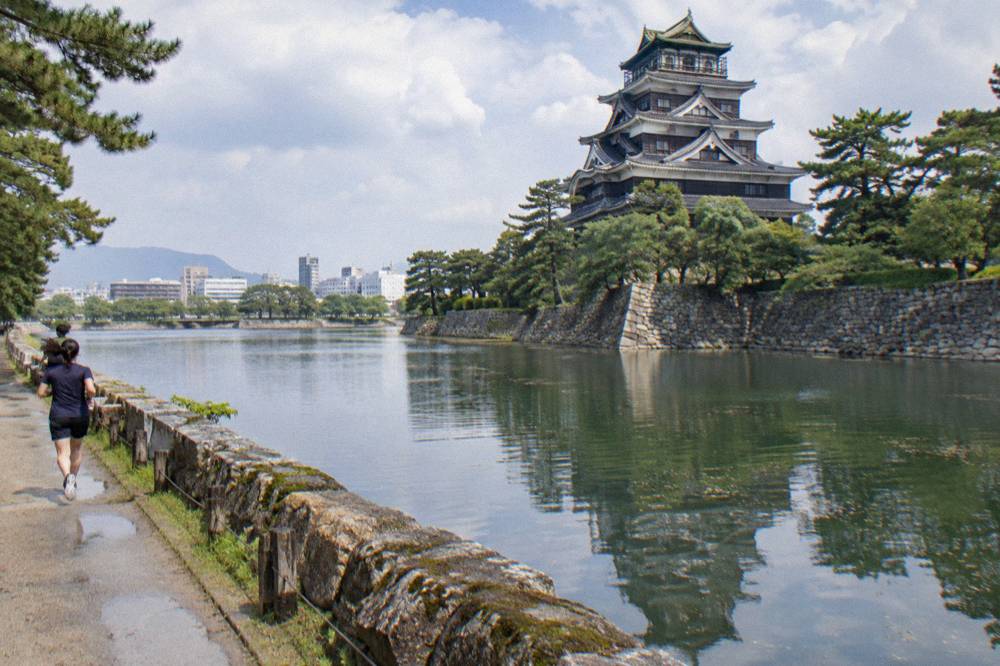 Hiroshima Castle keep reflected in its moat with stone walls in the foreground