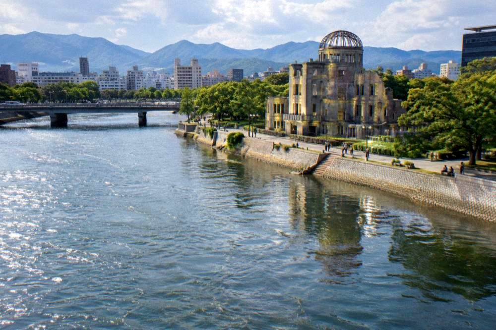An illuminated riverside promenade in Hiroshima with the lit dome reflected in the Motoyasu River