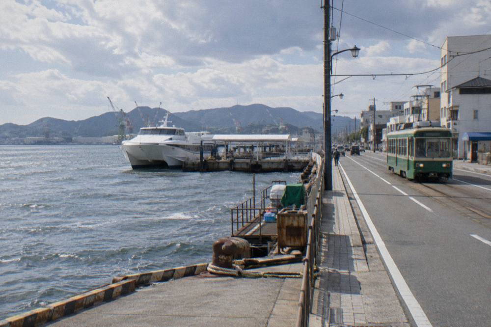 A green streetcar running along a city street with low buildings either side