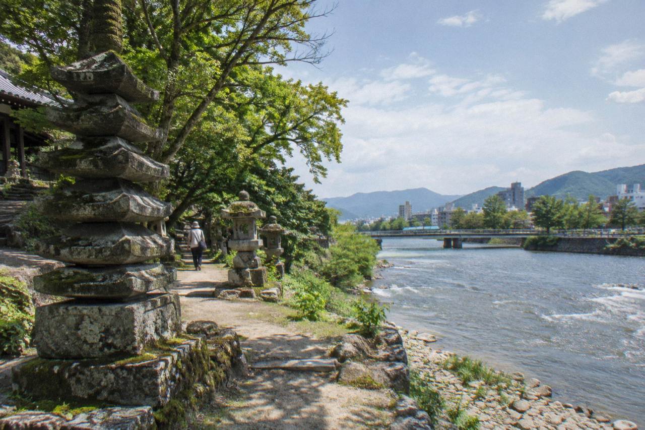 A quiet temple path with mossy stone pagodas beside a wooded stream in Hiroshima