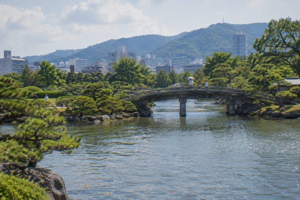 A landscaped Japanese garden pond with pines and a stone bridge in Hiroshima